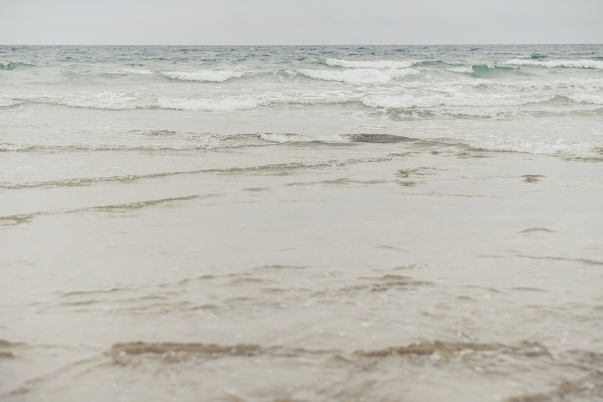 An image of shallow waves on a sandy shore. The weather is grey.